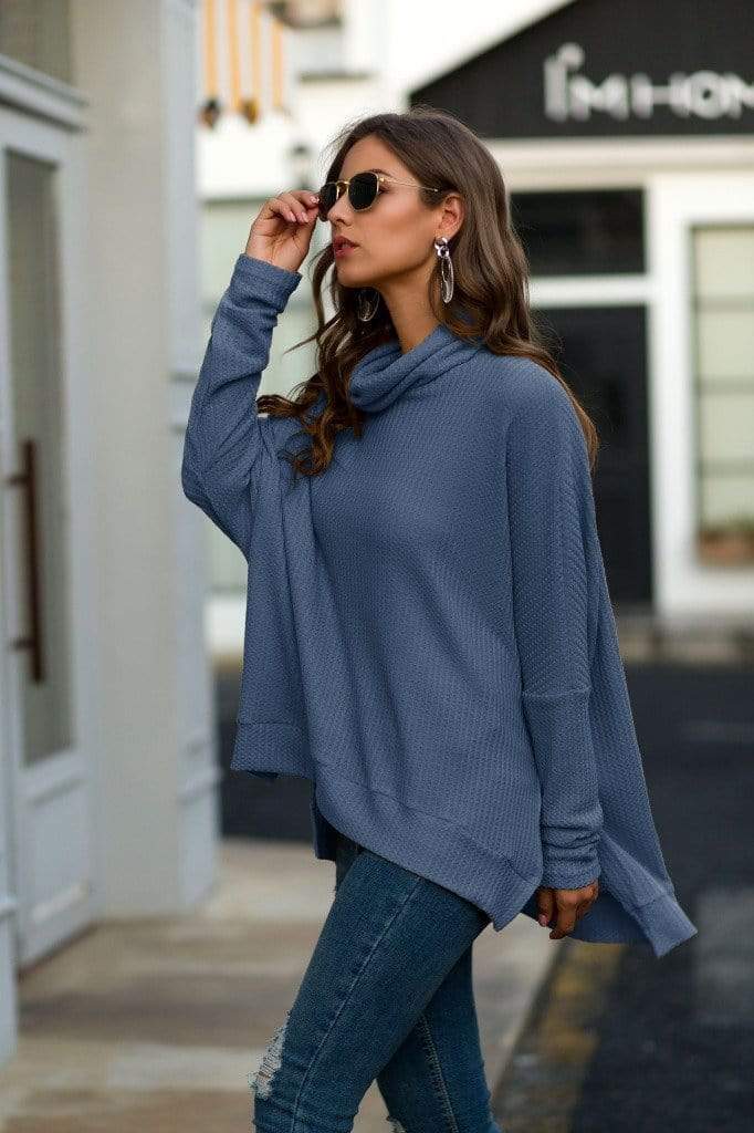 Woman wearing a blue sweater and jeans on a city street.