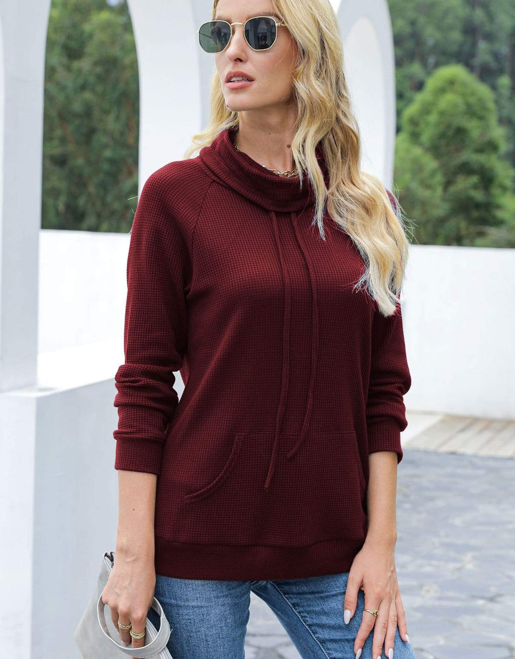 Woman wearing a burgundy cowl-neck sweater and sunglasses outdoors.