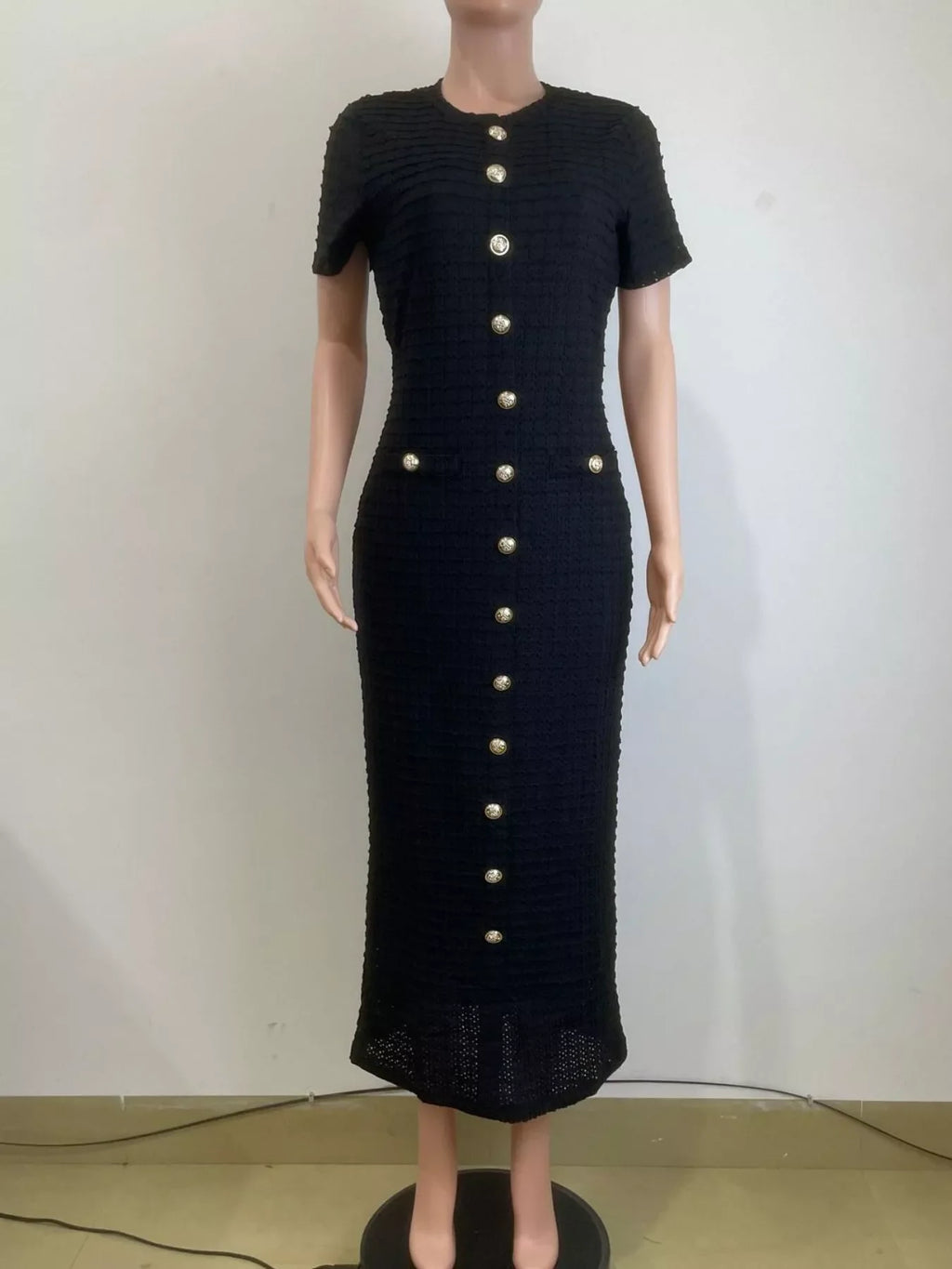 Black dress with gold buttons on a mannequin against a white background