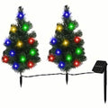Two small artificial trees with colorful lights and a solar panel on a white background